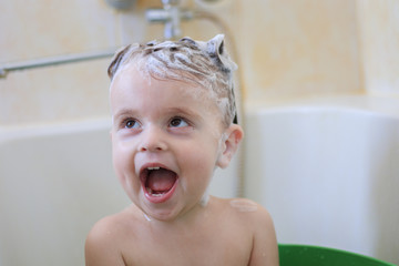 Cute little girl sitting in bath and laughing with shampoo on her head