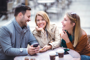 Group of three friends using phone in outdoor cafe on sunny day