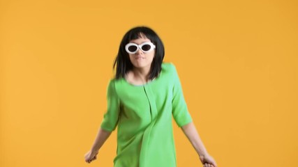 Portrait closeup of joyful retro girl with bob hairstyle wearing sunglasses dancing disco and doing energetic movements, over yellow background. Concept of emotions