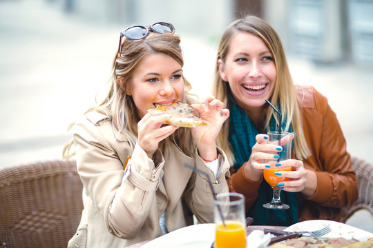 Portrait of two young women meating in cafe eating pizza outdoors,having fun together.