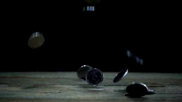 Slow motion, a pile of coins falls on a wooden table on a black background. Ukrainian coins in denomination of five kopecks are falling into a heap