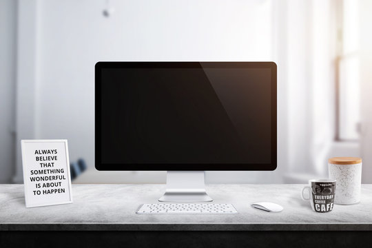 Modern computer display on office desk. Picture frame, box and coffee mug beside.