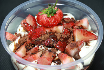 Home made cake and white buttercream, topping by Strawberries cut into pieces with cocoa powder in the round plastic cup.