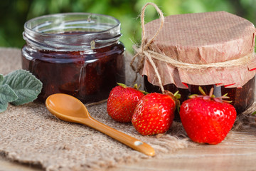 Traditional homemade strawberry jam in jars with fresh strawberries on wooden desk