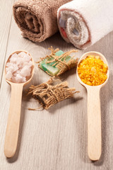 Wooden spoons with white and yellow sea salt and handmade soap for bathroom procedures with towels on the background