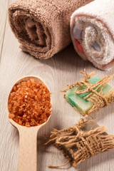 Wooden spoon with brown sea salt and handmade soap for bathroom procedures with towels on the background
