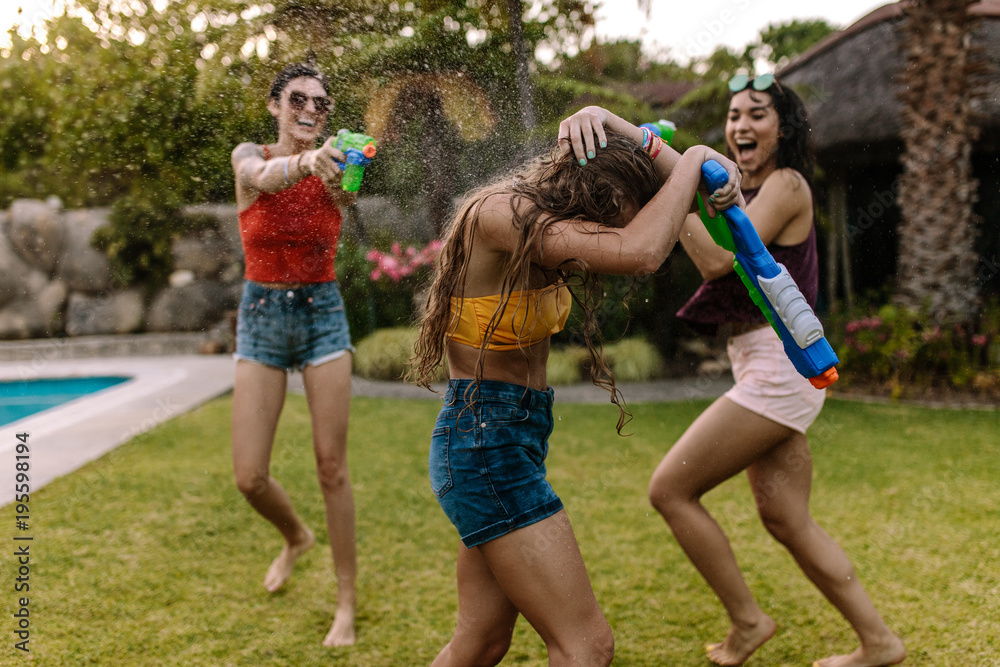 Wall mural Crazy female friends having water gun battle