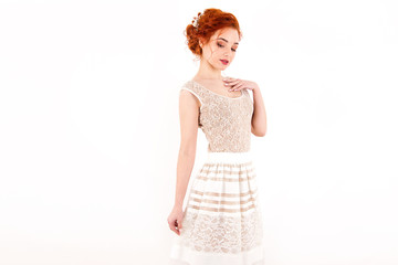 young girl with red hair in a beige lace dress standing on a white wall background