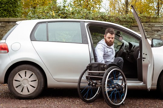 Disabled man holding wheelchair while boarding in his car