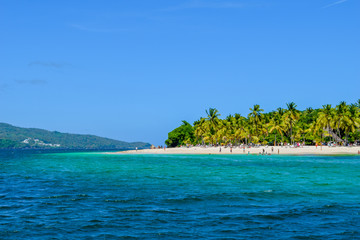 Beautiful beach with palms, blue sky and turquoise water, some tourists having fun, relaxing and swimming in the ocean, caribbean sea