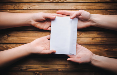 Hands pass the white envelope to the other hands on a wooden background. Transfer of money for donation.