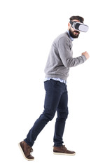 Naklejka premium Side view of young bearded smart casual man with vr glasses running astonished and looking at camera. Full body isolated on white background. 