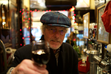 Mature Man in Harris Tweed Hat - holding glass of red wine, at bar