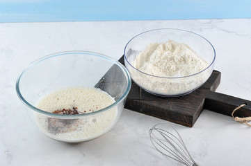 Mixes for baking. In one bowl, flour. In another beaten egg with sugar and liquid chocolate to get the chocolate dough. In the frame, whisk for whipping. Light background. Close-up.