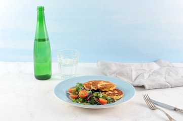 Potato cutlets and lettuce with cherry tomatoes. Proper nutrition, ideal for vegetarians. Next to the plate are cutlery and napkins. In the frame, a bottle and a glass of water. Light background. 