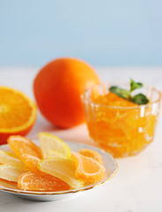 Orange jam and marmalade in the form of orange and lemon slices. Next to an orange and half an orange. Light background. Close-up. Vertical orientation of the frame.