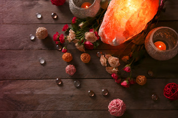 Himalayan salt lamp, candles and flowers on wooden table