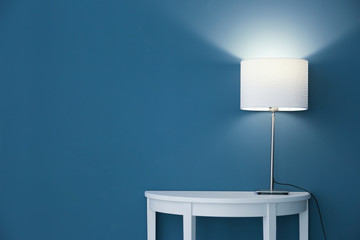 Elegant lamp on table near color wall