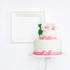 Cake decorated with roses and pink bows on stand with frame on white background