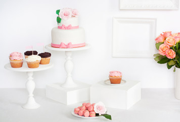 Cake decorated with roses and bows with cupcakes and macarons standing on a table