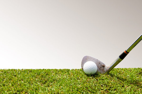Golf club and golf ball in grass with copy space on gray background.