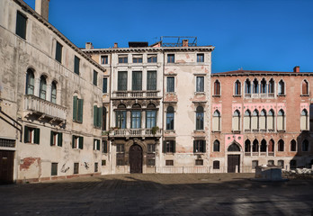 Fototapeta na wymiar historic Venetian residences in a sunny square with a well and the tables of a cafe. Venice, Italy