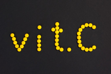 Top view of  inscription “vit. C” made of yellow pills on black background.