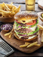 Big hamburger and French fries on the wooden tray.
