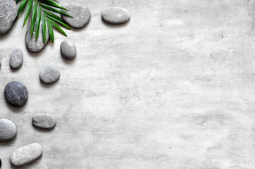Obraz na płótnie Canvas Grey spa background, palm leaves and grey stones, top view