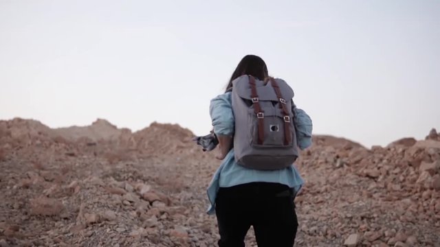 Woman hikes up on a steep rocky hill. Slow motion. Tourist girl climbs mountain with big stones. Hard way to the top.