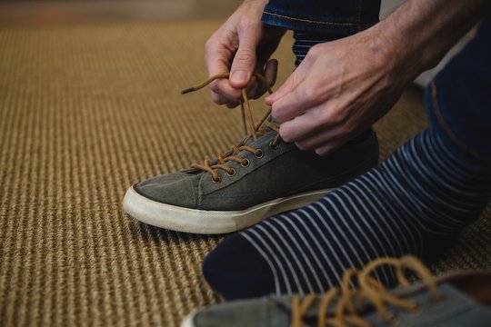 Man Tying Shoelaces In Living Room At Home