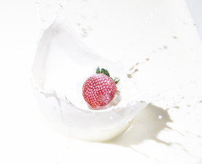 Strawberry falling into splashing milk.
