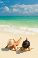 Sexy bikini body of two women enjoy the sea by laying down on sand of beach wearing hat. Happy island lifestyle. White sand and crystal sea of tropical beach.