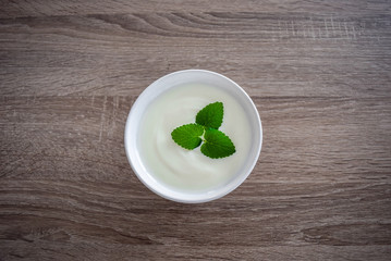 Ceramic bowl of white yogurt with mint leaves as decoration isolated on vintage rustic wooden table from top view, plain yoghurt