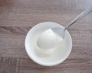 Bowl of white yogurt with spoon isolated on vintage rustic wooden table from above, plain yoghurt