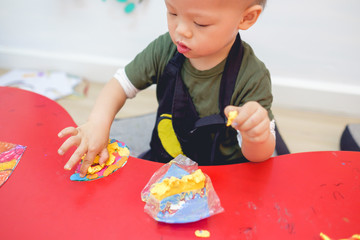 Cute Asian 18 months old toddler boy child playing modeling clay / play dought at play school,...