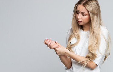 Young cute blonde Caucasian woman holding her painful wrist caused by prolonged work on the...