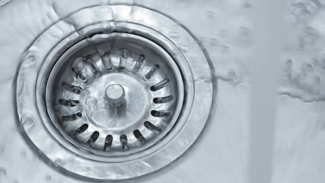 Streaming water in sink. Water stream going down the drain.
