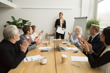 Senior and young businesspeople applauding businesswoman after presentation at conference meeting,...