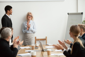 Smiling senior businesswoman boss and team clapping hands at meeting, happy woman executive...