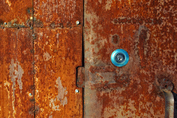 Old very rusty metal door background texture with new stainless keyhole, color palette from bright orange to dark brown