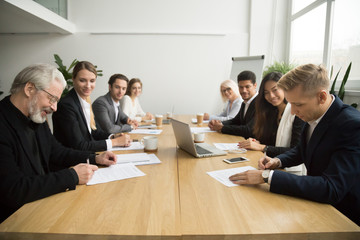 Senior and young businessmen sign contracts at group multiracial meeting, experienced investor buying startup making partnership deal after successful negotiation putting signature on business papers