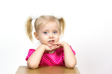 A beautiful young blond girl leans her elbows on a chair and puts her head on her hands. Little girl 3 years old on a white background put her head on her hands.