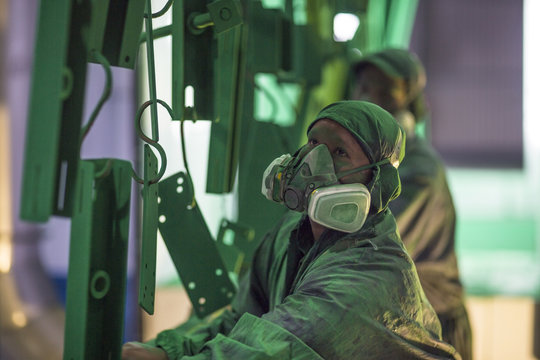 Workers wearing protective masks spraying metal