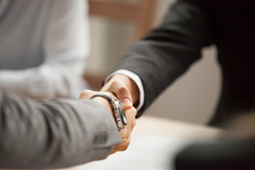 Obraz na płótnie Canvas Two businessmen in suits shaking hands at group meeting, partners handshaking at negotiations making deal or signing contract, thanking for help support, welcome greeting handshake concept, close up