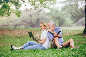Fototapeta premium Elderly couple using a laptop while sitting on grass in the park