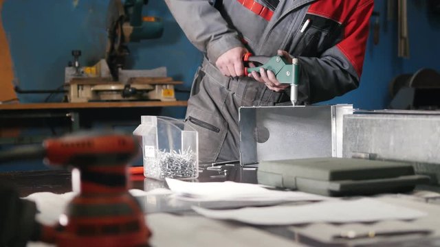 Worker assembling the metal part by hand with pliers, tools for grinding metal and metal details in the foreground