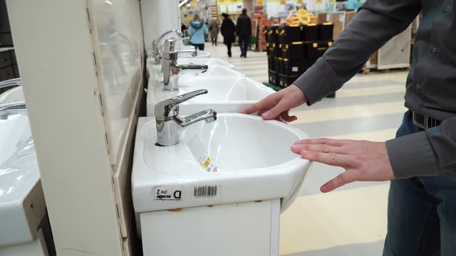 Young man selecting bathroom sink and furniture at store. Guy examining new sink