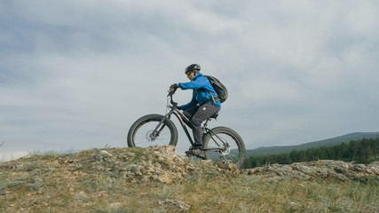 Naklejka premium Fat bike also called fatbike or fat-tire bike in summer driving through the hills. The guy is riding a bike along the sand and grass high in the mountains. He performs some tricks and runs dangerously