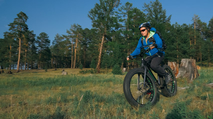Naklejka premium Fat bike also called fatbike or fat-tire bike in summer riding in the forest. The guy rides a bicycle among trees and stumps. He overcomes some obstacles on a bumpy road.